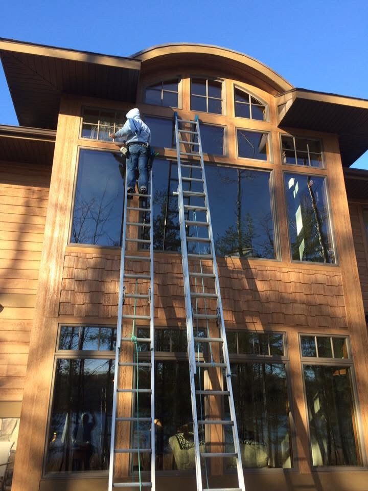 Premier Window Cleaning crew cleaning second-story windows on a northern Michigan home at golden hour